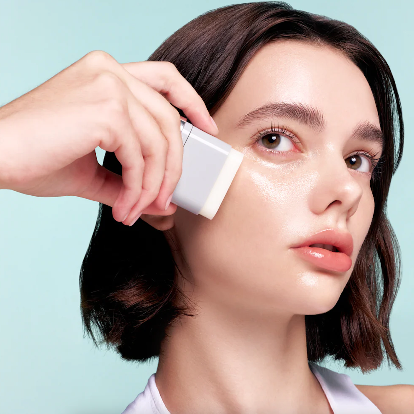 Woman applying VT PDRN Essence Stick Balm  to her face with a light blue background