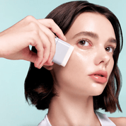 Woman applying VT PDRN Essence Stick Balm  to her face with a light blue background