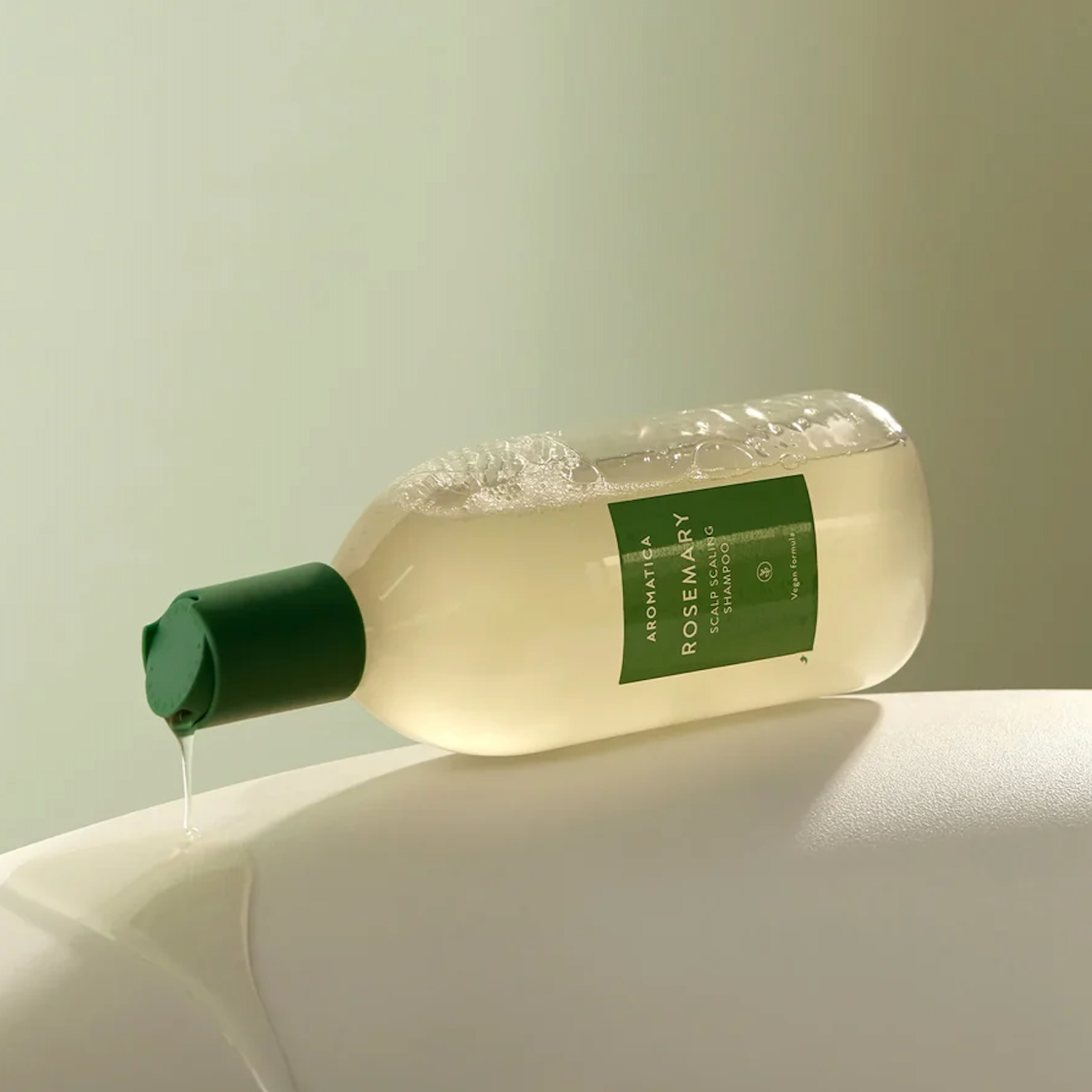 Bottle of Aaromatica Rosemary Scalp Scaling shampoo with a green cap on a light surface.