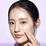 Woman applying cream to her face with a light purple background
