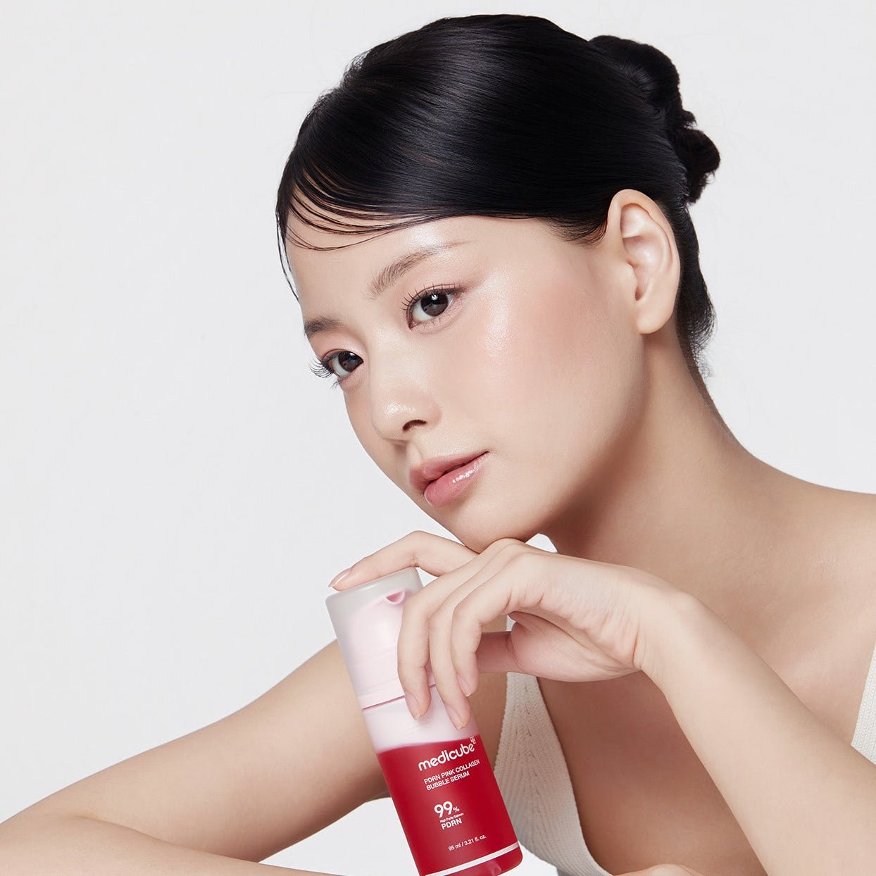 Women holding the MEDICUBE PDRN Pink Collagen Bubble Serum bottle on white background